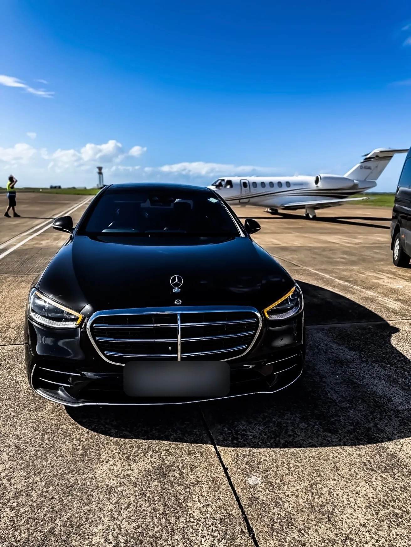 Black Mercedes S-Class parked on an airfield apron beside a private jet
